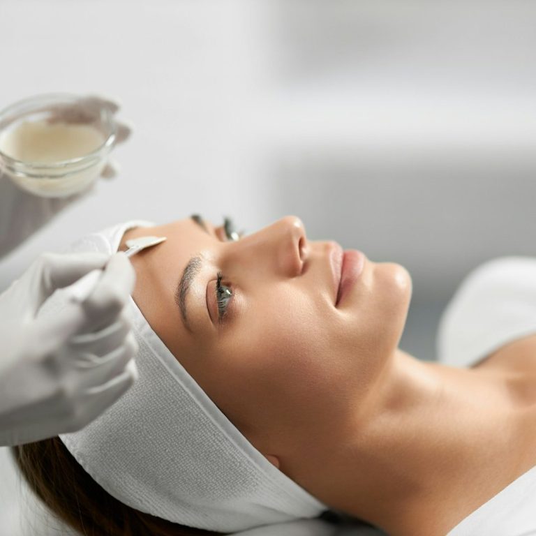 Vrouw ontvangt een huidverzorgende behandeling waarbij een serum met een waaierpenseel zorgvuldig op haar gezicht wordt aangebracht bij Just